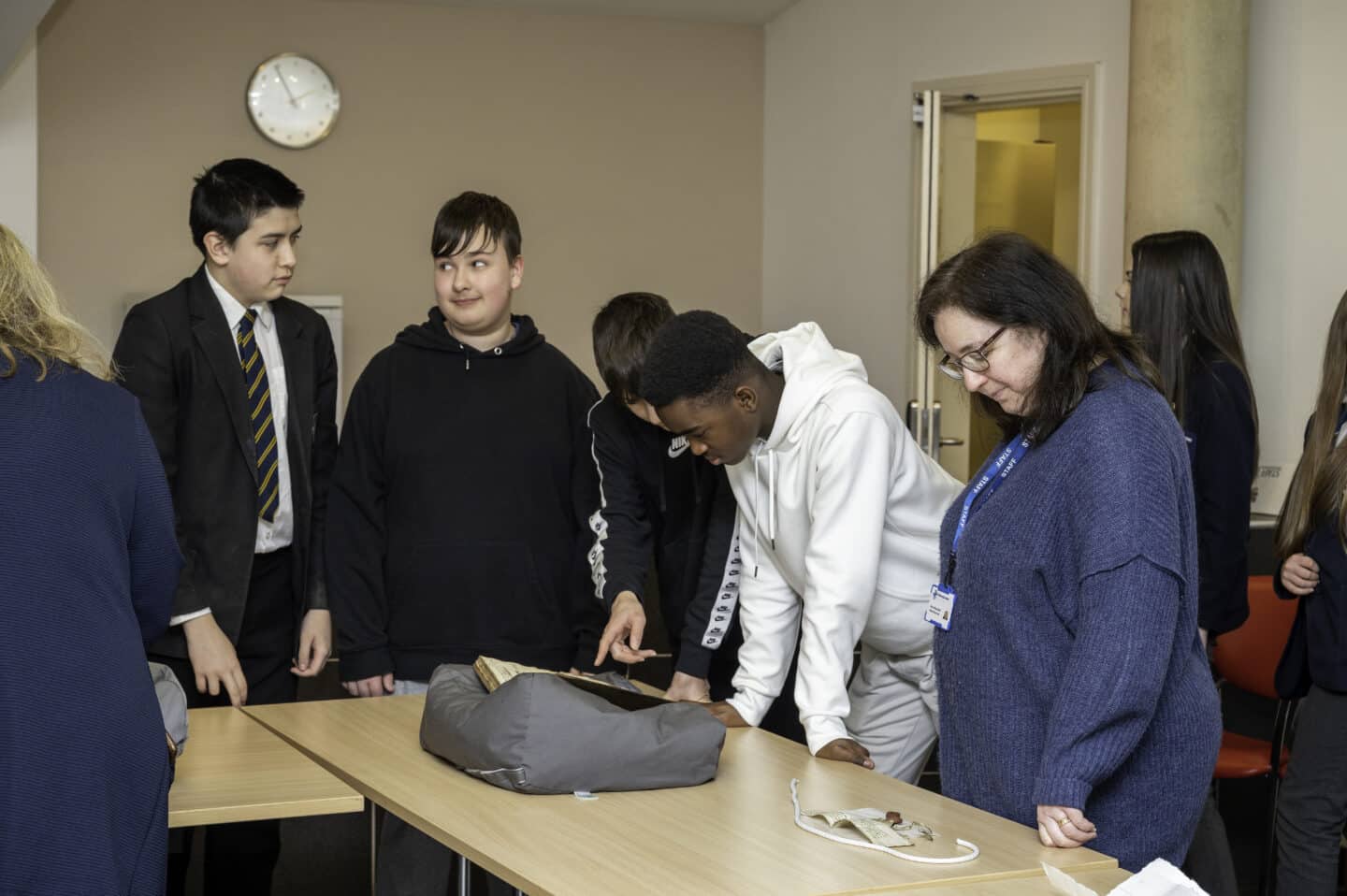 A group of young students and their teacher looking at a manuscript and other items on a table