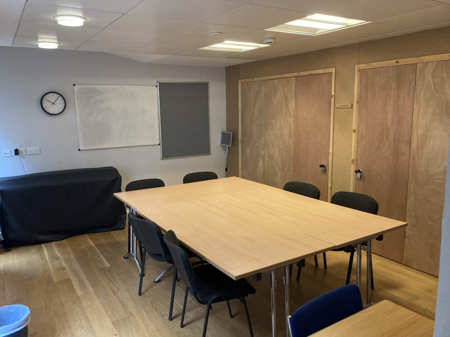 Image of the Lincoln College Courtyard Room, with a large table, chairs, a whiteboard, and a clock.