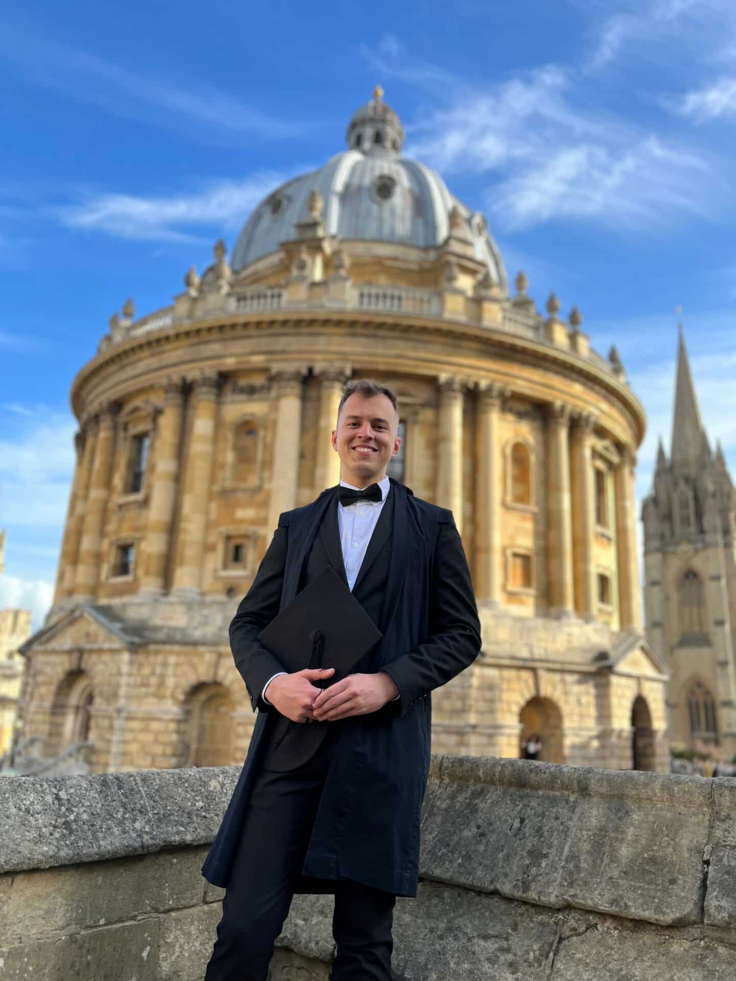 A young man, Denys Karlovskyi, in sub fusc standing in front of the Oxford Radcliffe Camera