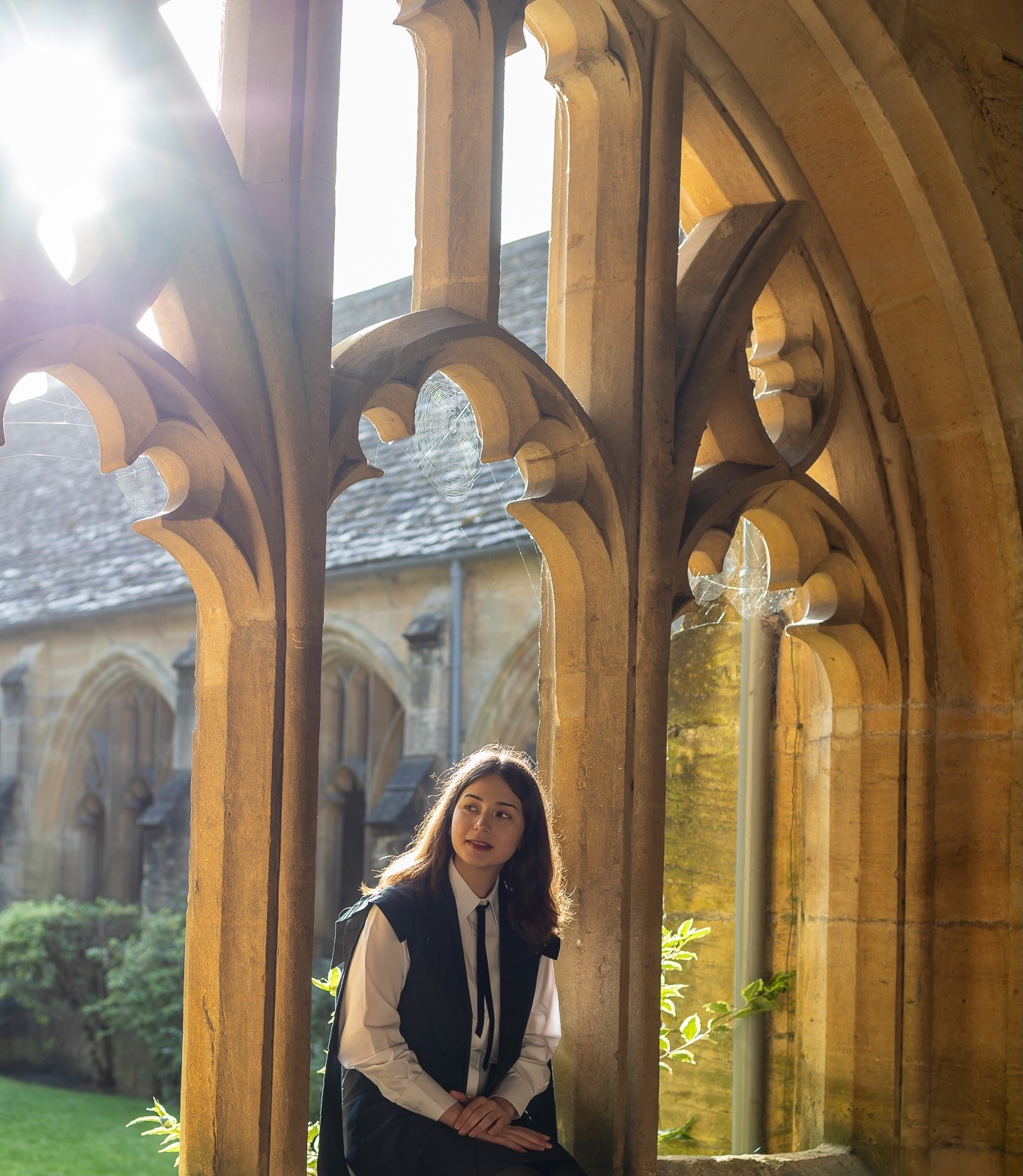 Photograph of Elif Bayat in subfusc, sitting among cloisters