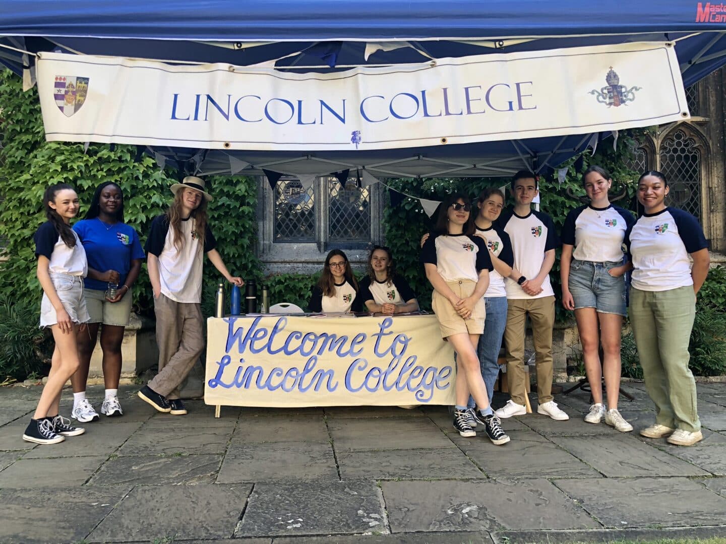 A group of student ambassadors at Open Day with a sign saying "Welcome to Lincoln College"