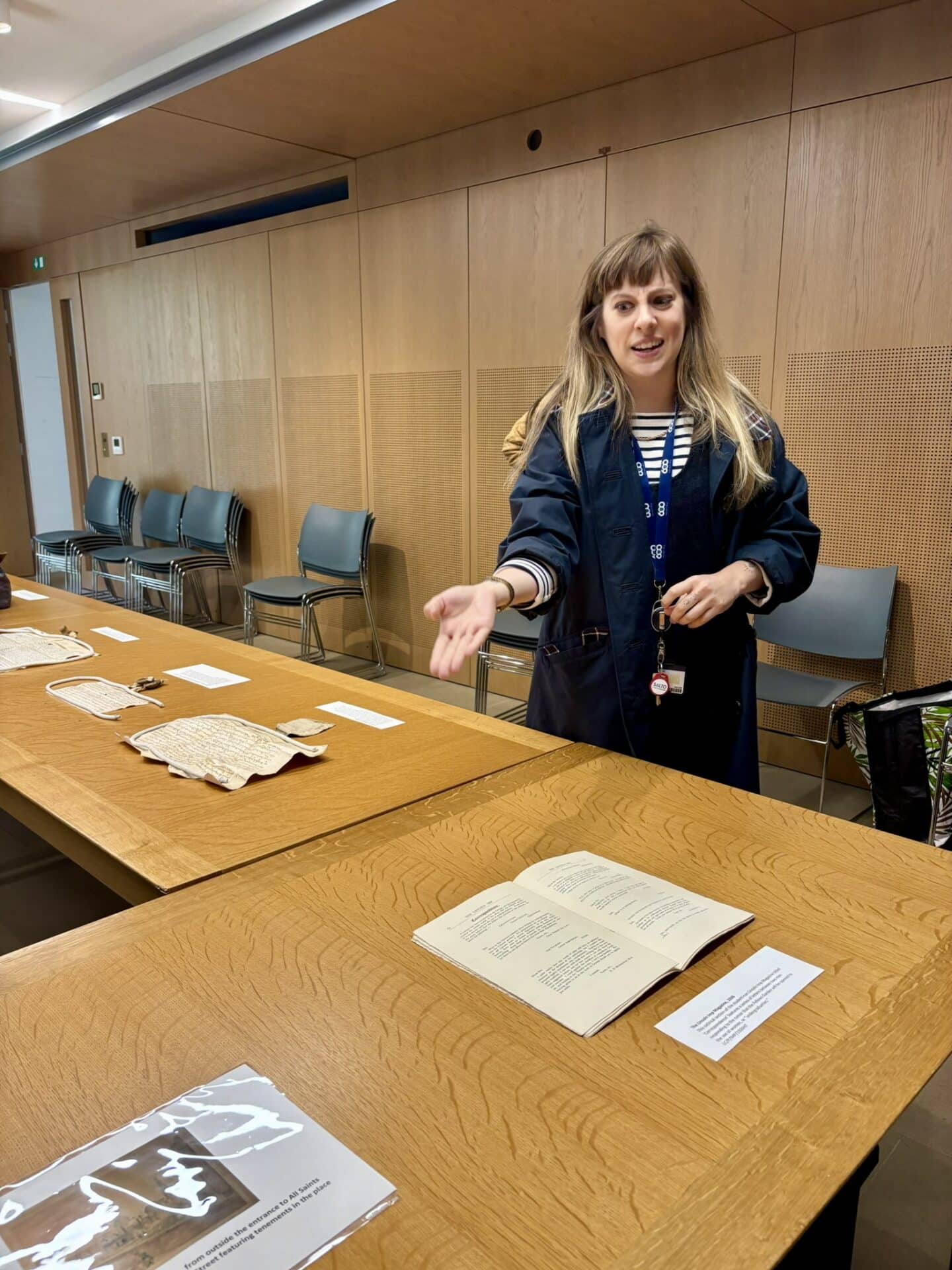 Alison Ray, Lincoln College Archivist, presenting historical documents laid out on a wooden table during a display session. She gestures while speaking, with archival materials including manuscripts and printed texts visible in front of her.