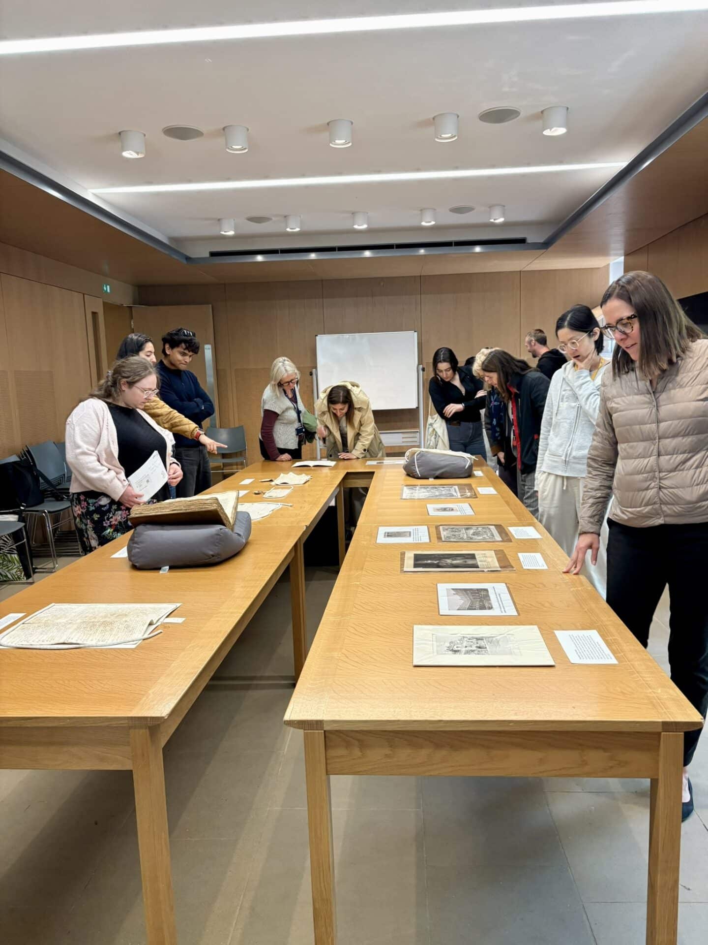 “Lincoln College staff and students examining archival materials displayed on wooden tables in a seminar room. The group is engaged in viewing historic documents, prints, and manuscripts.