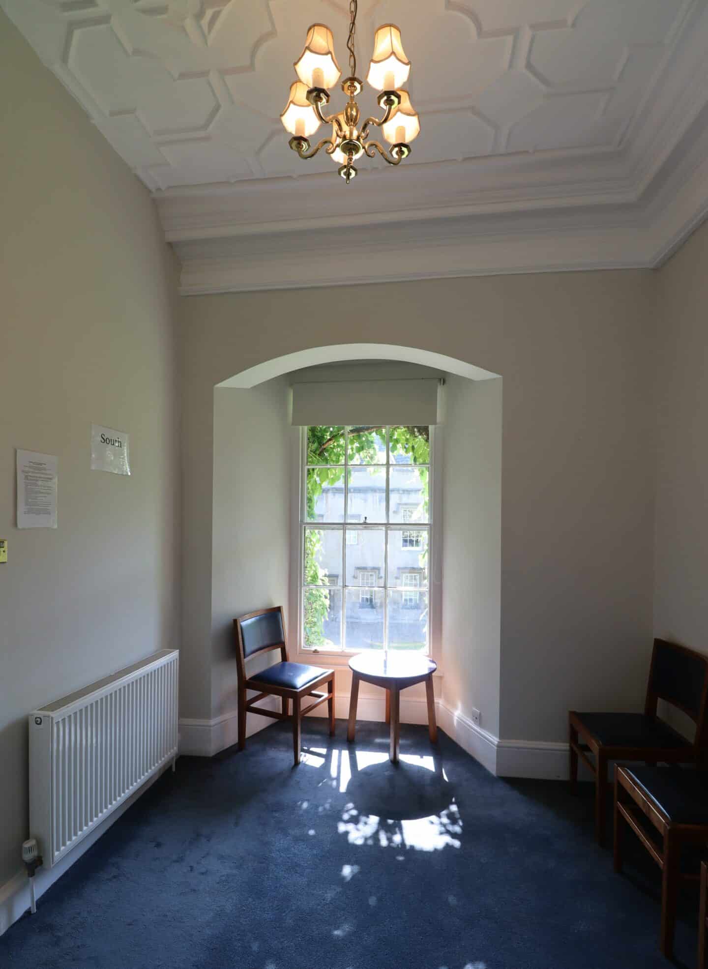 Photo of prayer room showing chairs and an end table with the sun streaming from a tall window