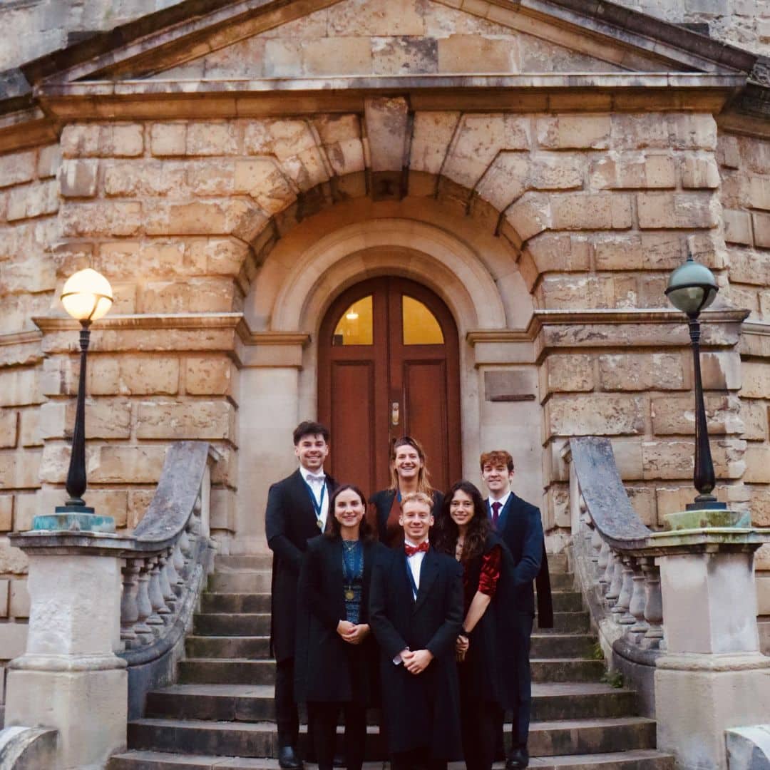 Running Club members standing at the bottom of staircase wearing black formal suits