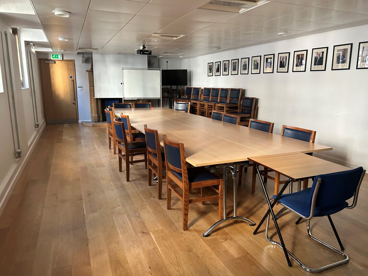 Photograph of the Turl Yard Lecture Room, with a large table and chairs, a whiteboard, and a projector screen