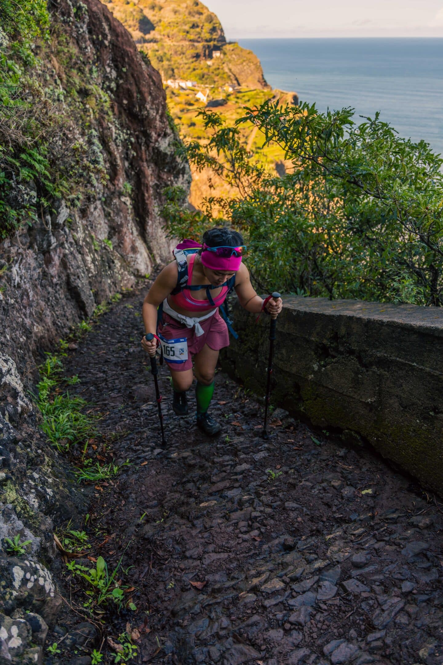 Micon Garvilles, running ultramarathon up a steep hill with poles in each hand and the ocean in the background
