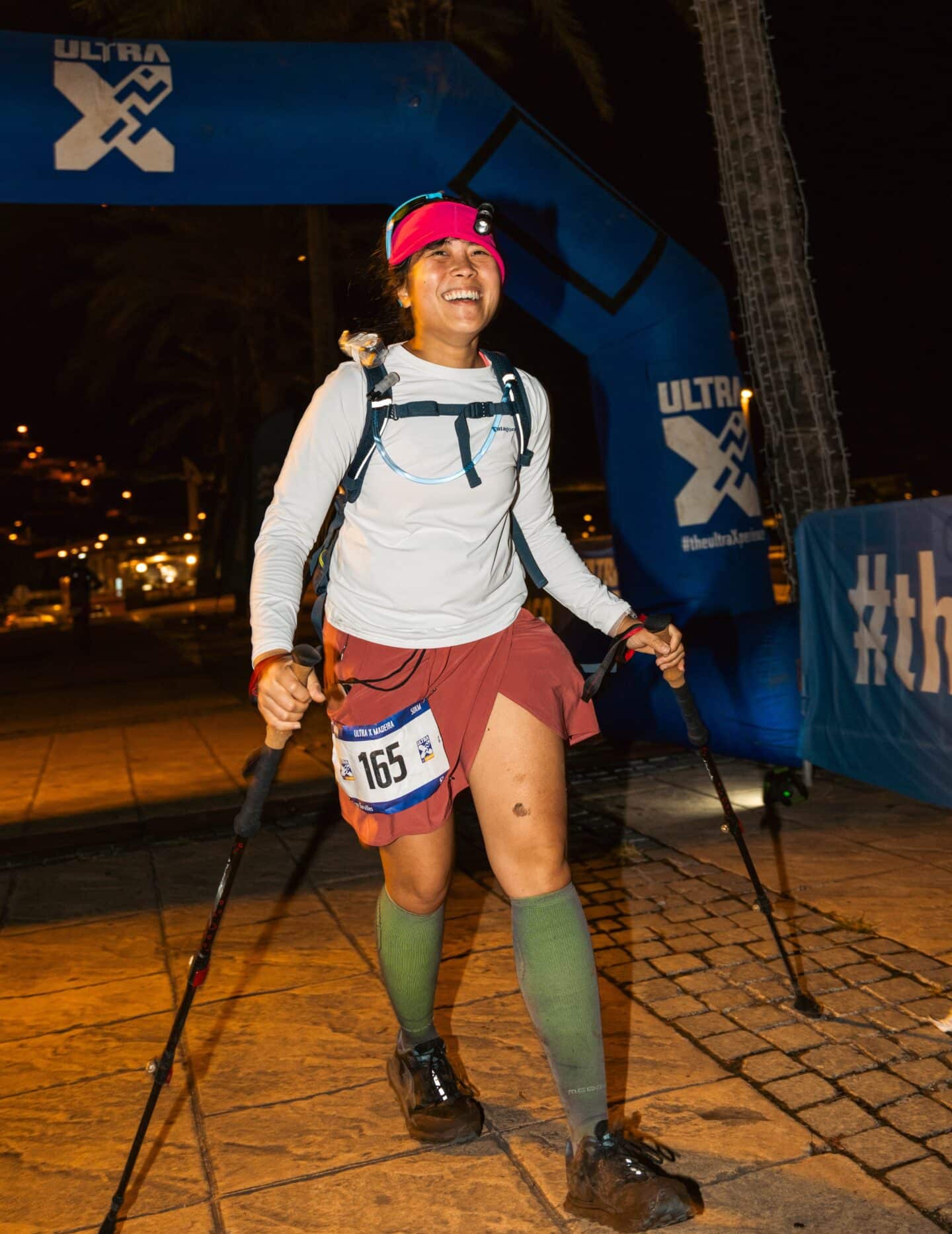 Micon Garvilles crossing the finishing line of the ultramarathon, wearing pink skort and green socks, and poles in each hand