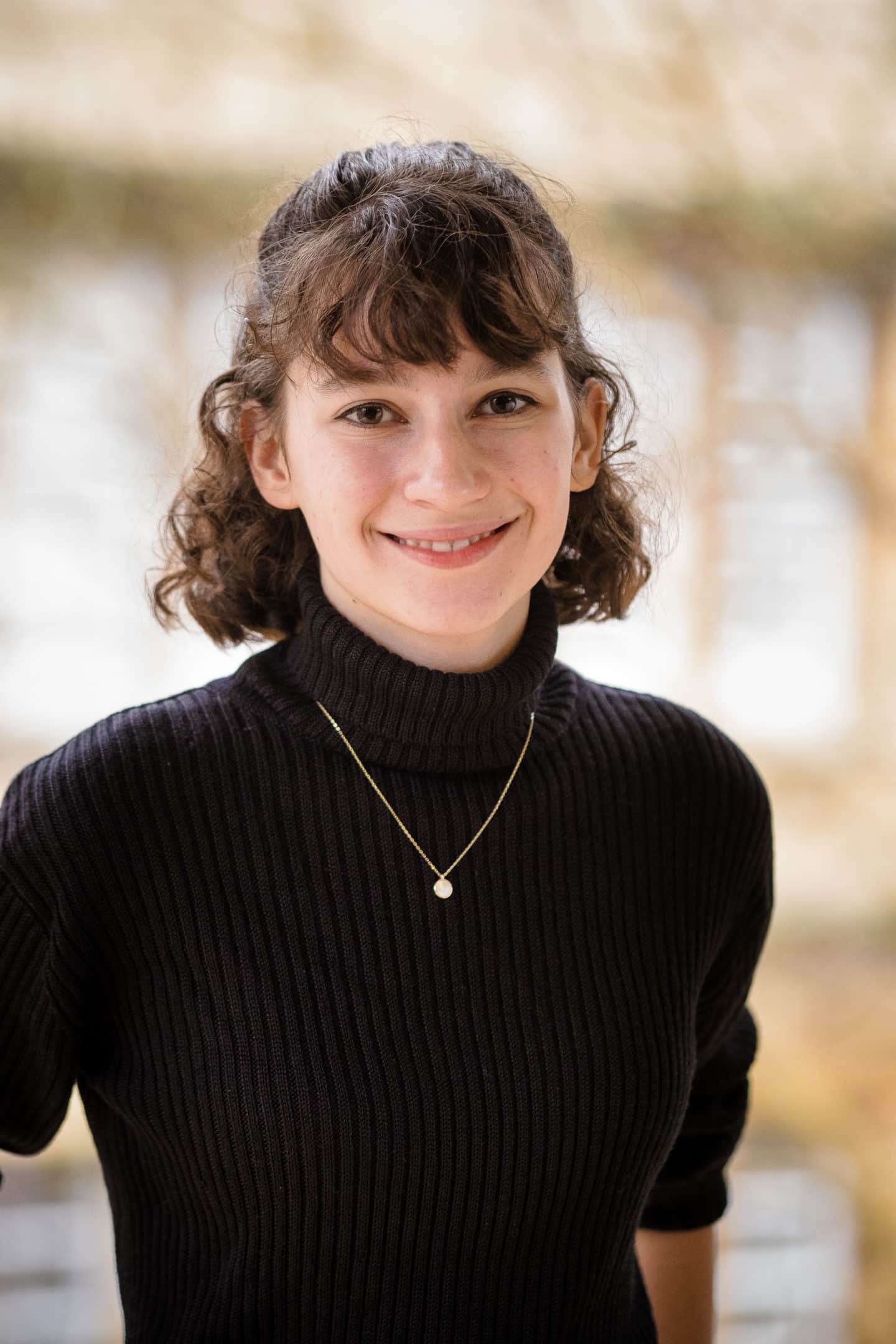 Headshot of Anna Gunstone, a young woman in a black jumper and a pendant necklace