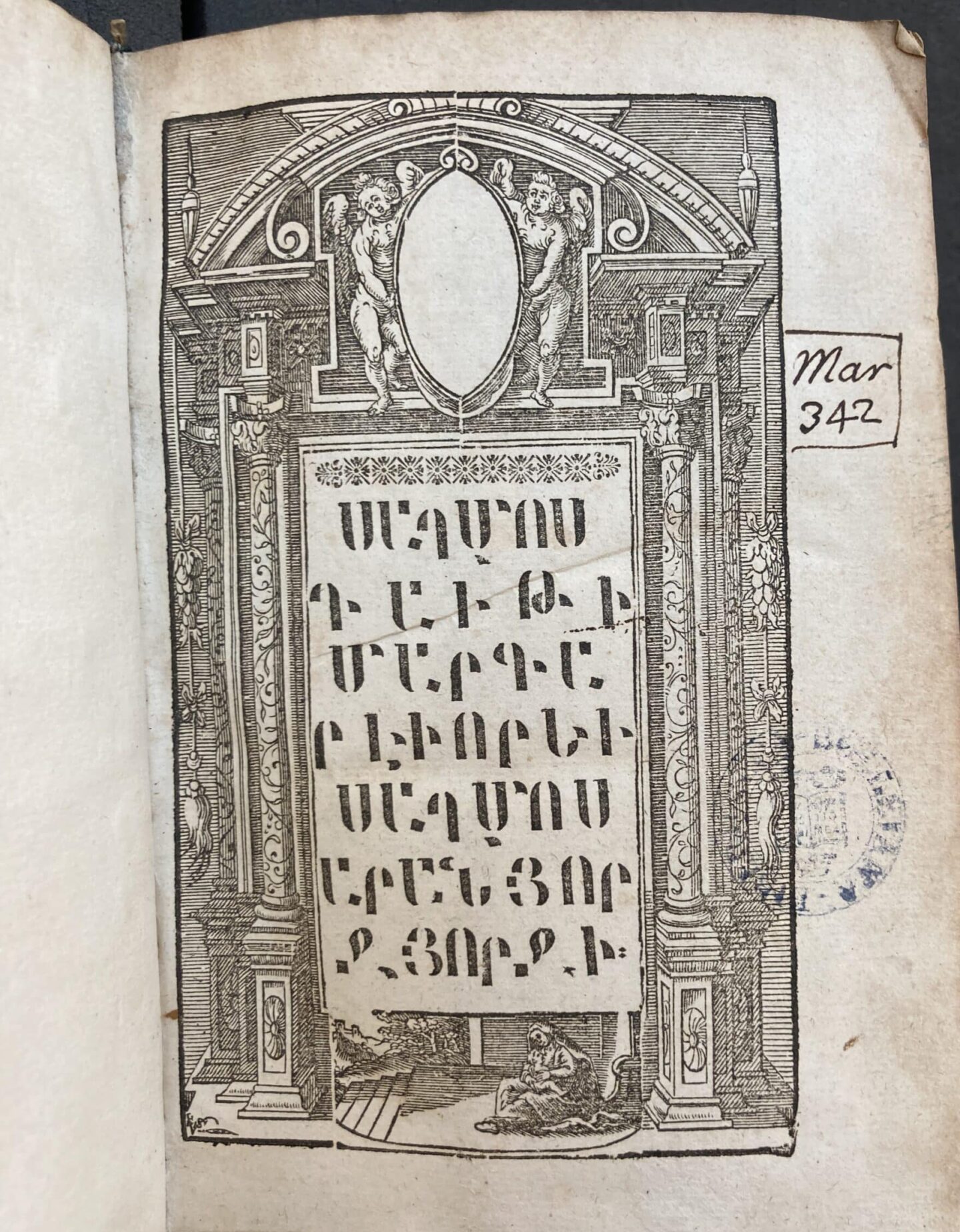 Printed title page of an Armenian Bible with large text in the middle, surrounded by an image of a columned building, with two Cupid-like figures holding a mirror at the top