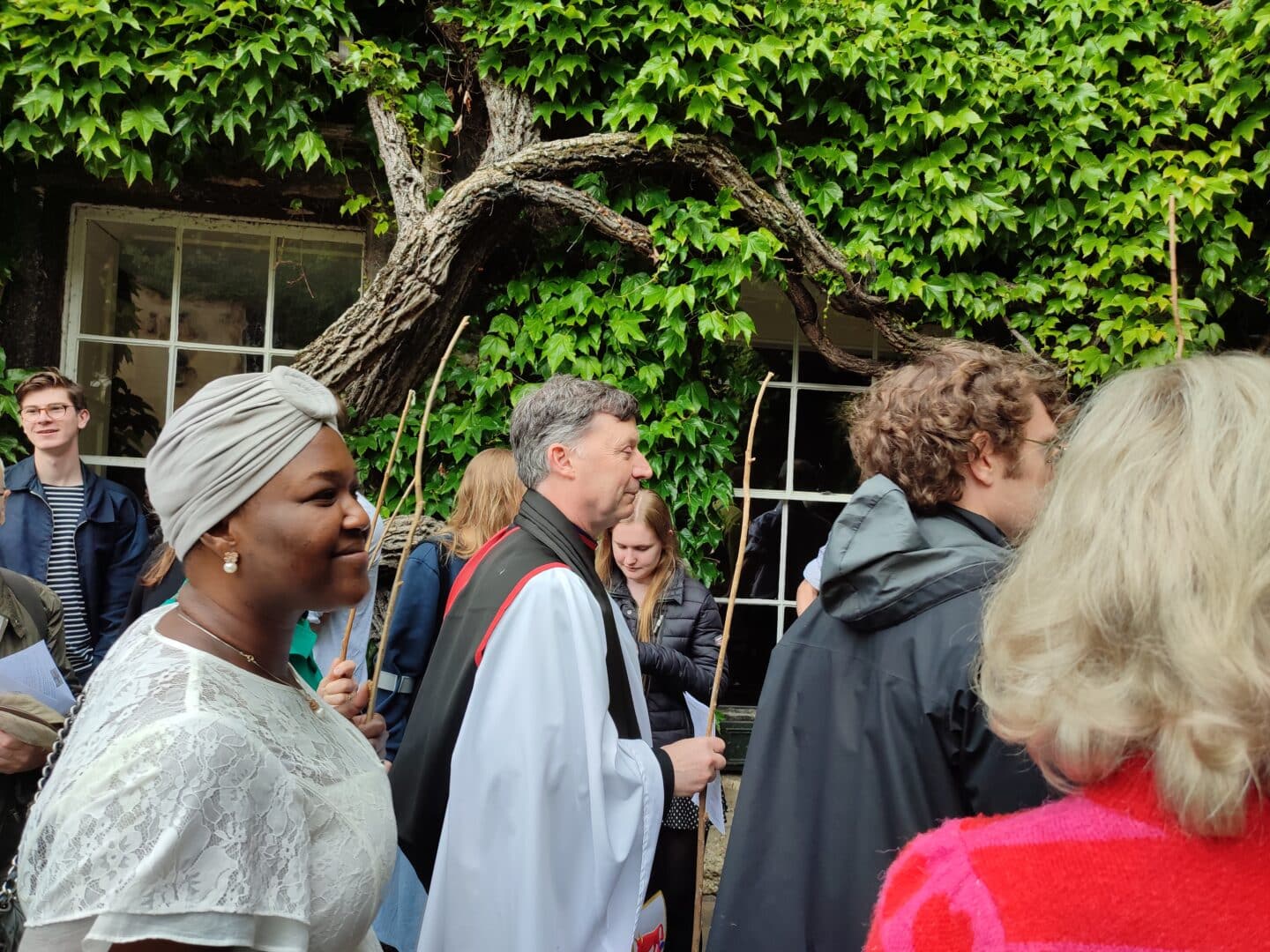 Photograph from Lincoln College on Ascension Day of a crowd of people, including one priest, bearing long thin sticks