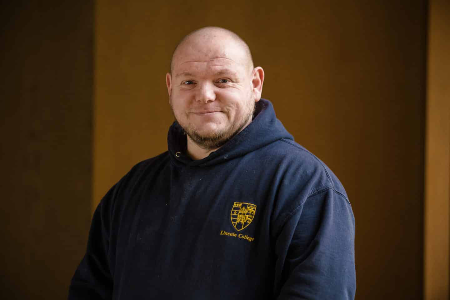 Headshot of David Gee, a man in a blue hoodie with the Lincoln College crest in gold