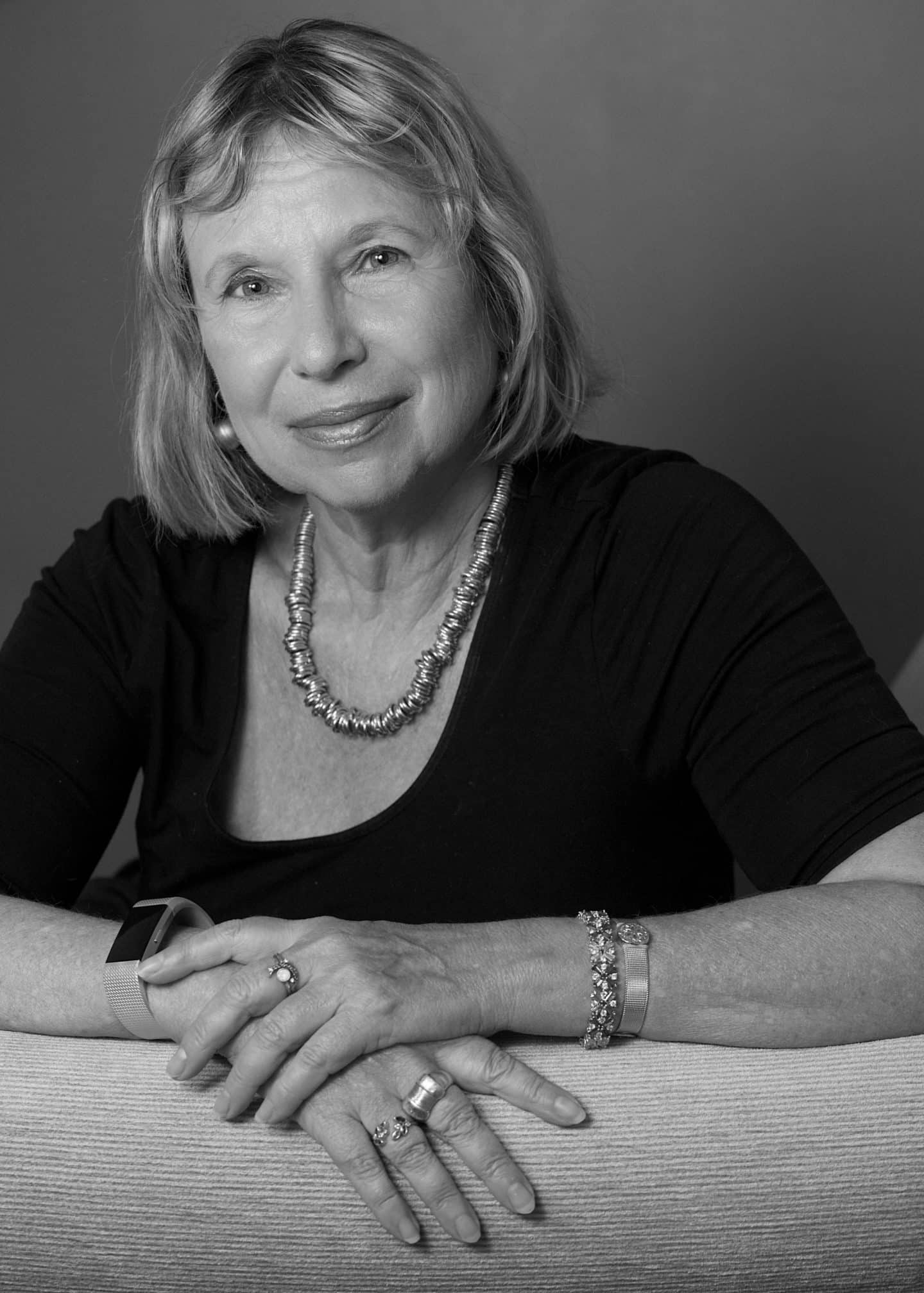 Greyscale photograph of Fania Oz Salzberger, a woman in a black top, necklace, bracelet, rings and watch