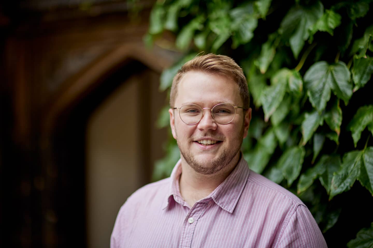 Headshot of George Booth, a man in glasses and a pink shirt