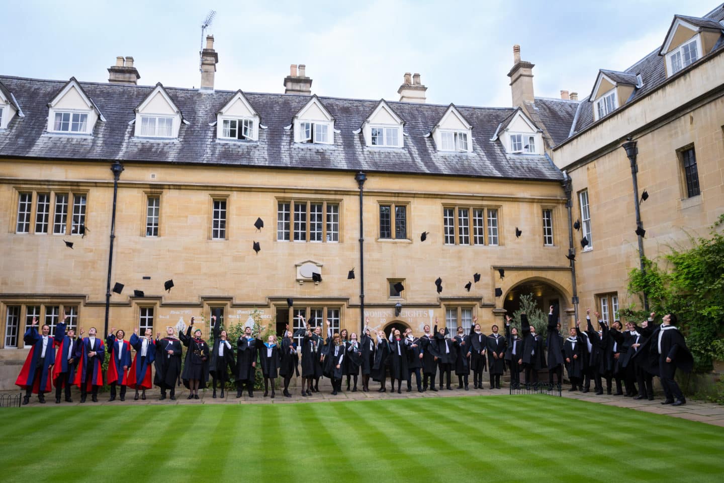 Students in their graduation gowns lined up around a Lincoln College Quad throwing their graduation caps in the air