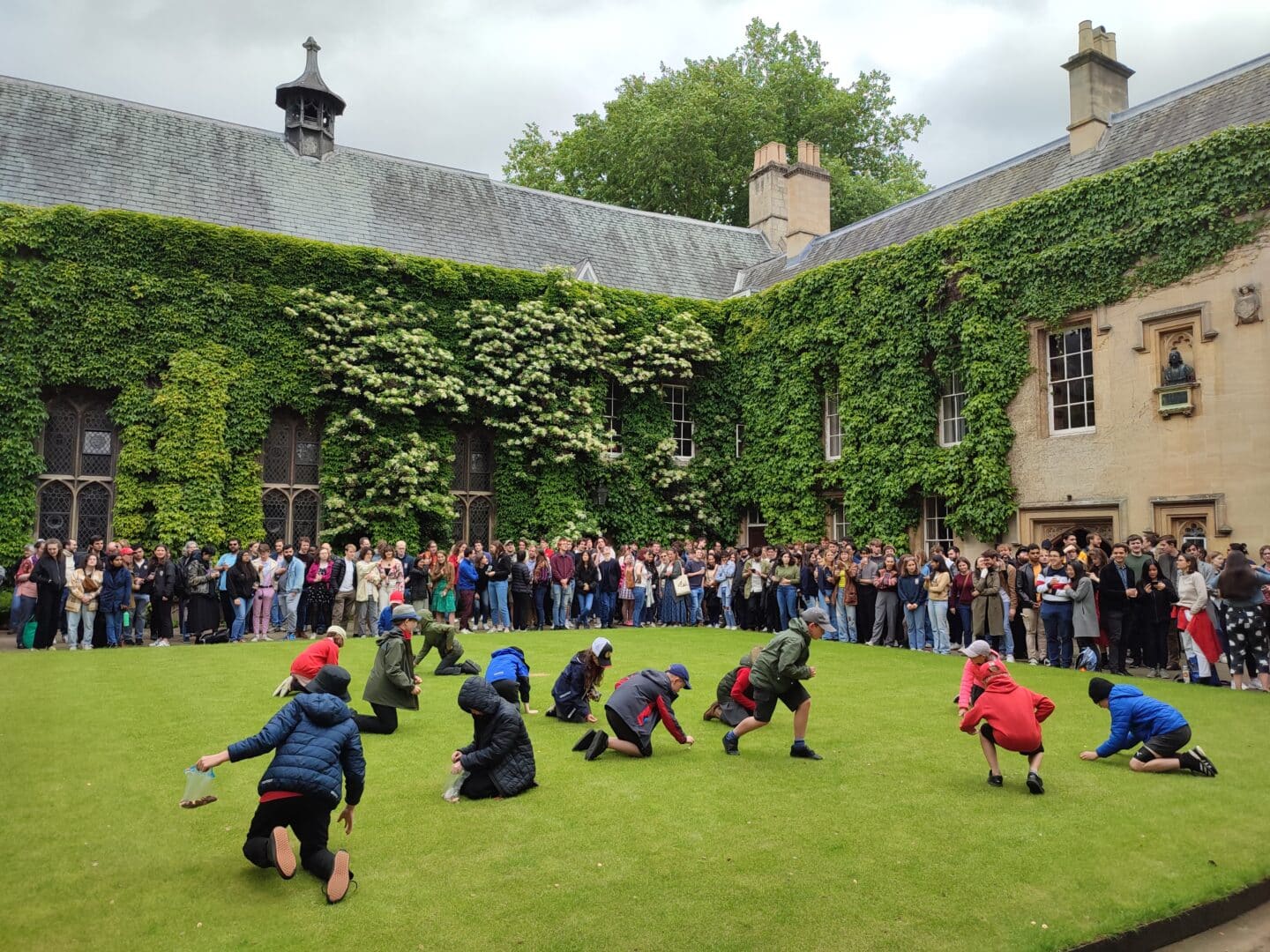 A photograph of the Lincoln Front Quad on Ascension Day, with a group of young schoolchildren on the grass, picking up pennies, while a large crowd looks on from the sides.