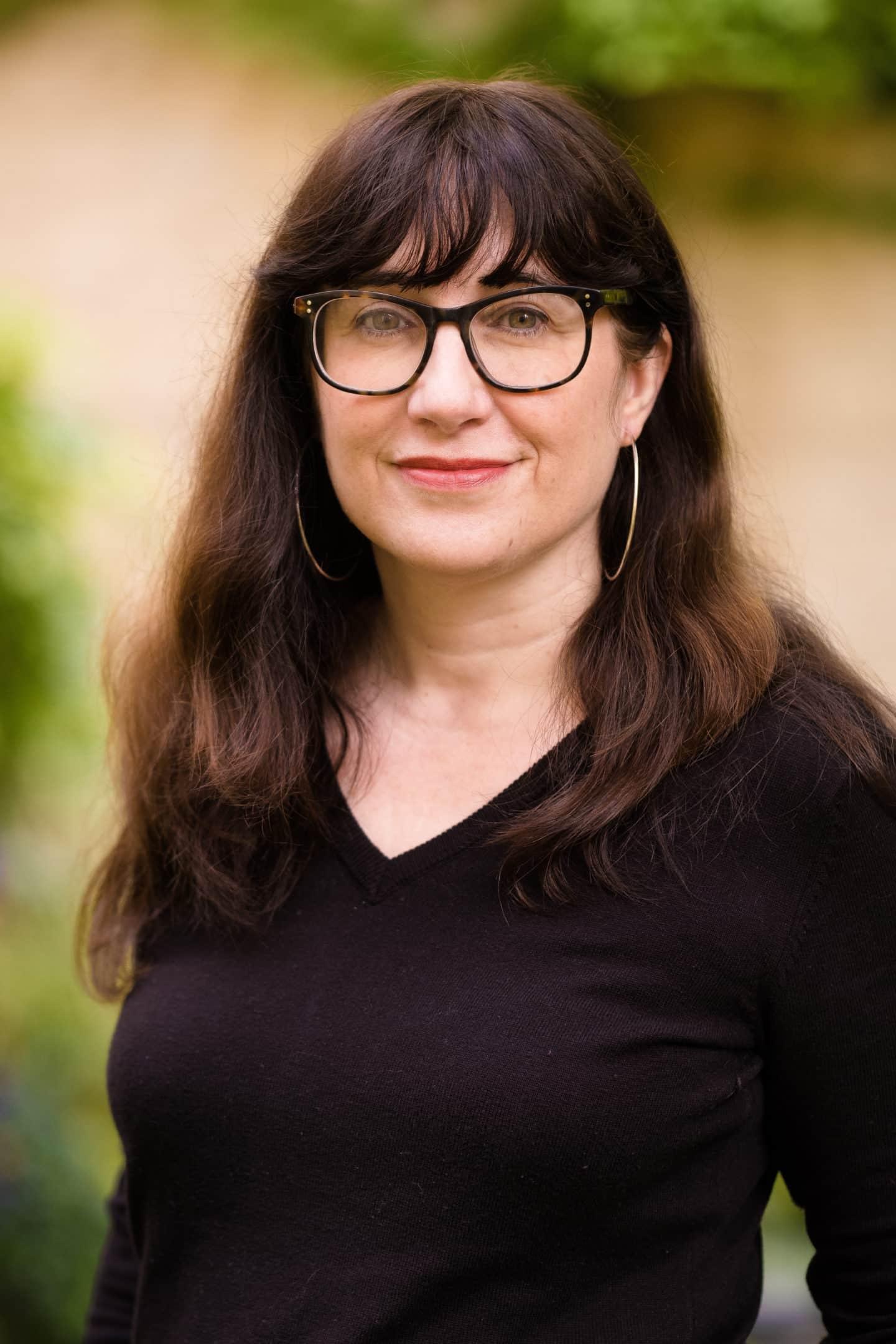 Headshot of Lisa Stokes-King, a woman in a black sweater, with glasses and hoop earrings