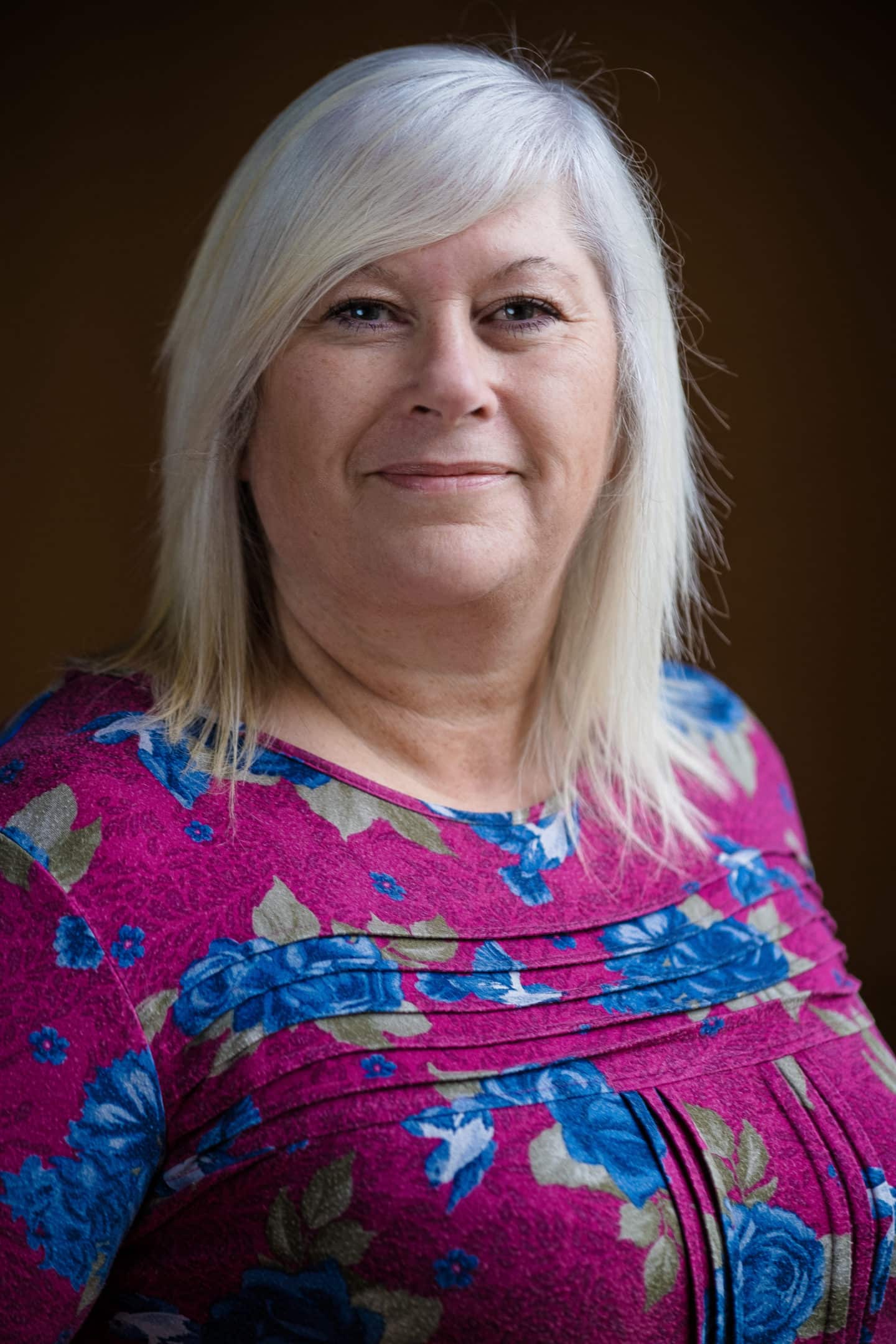 Headshot of Patricia Cripps, a woman in a pink and blue floral top