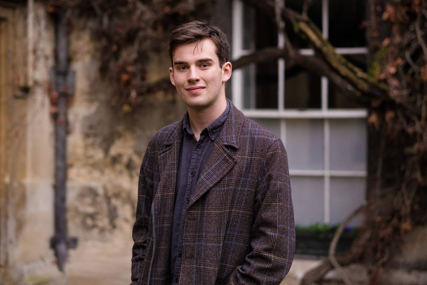 Photograph of Patrick Hayes, a young man in a shirt and brown coat