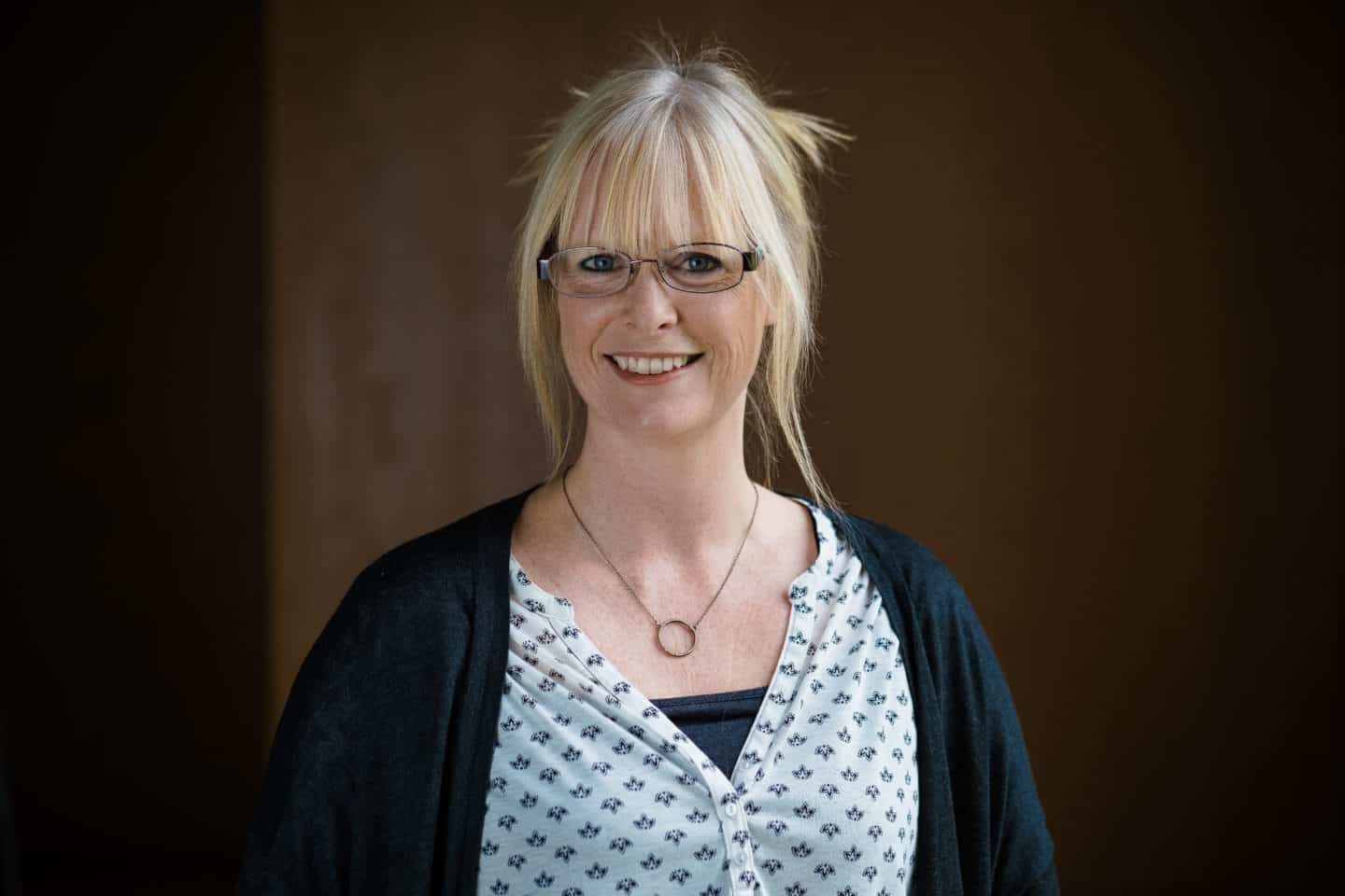 Headshot of Rachel King, a woman in glasses, a white top, dark cardigan and necklace