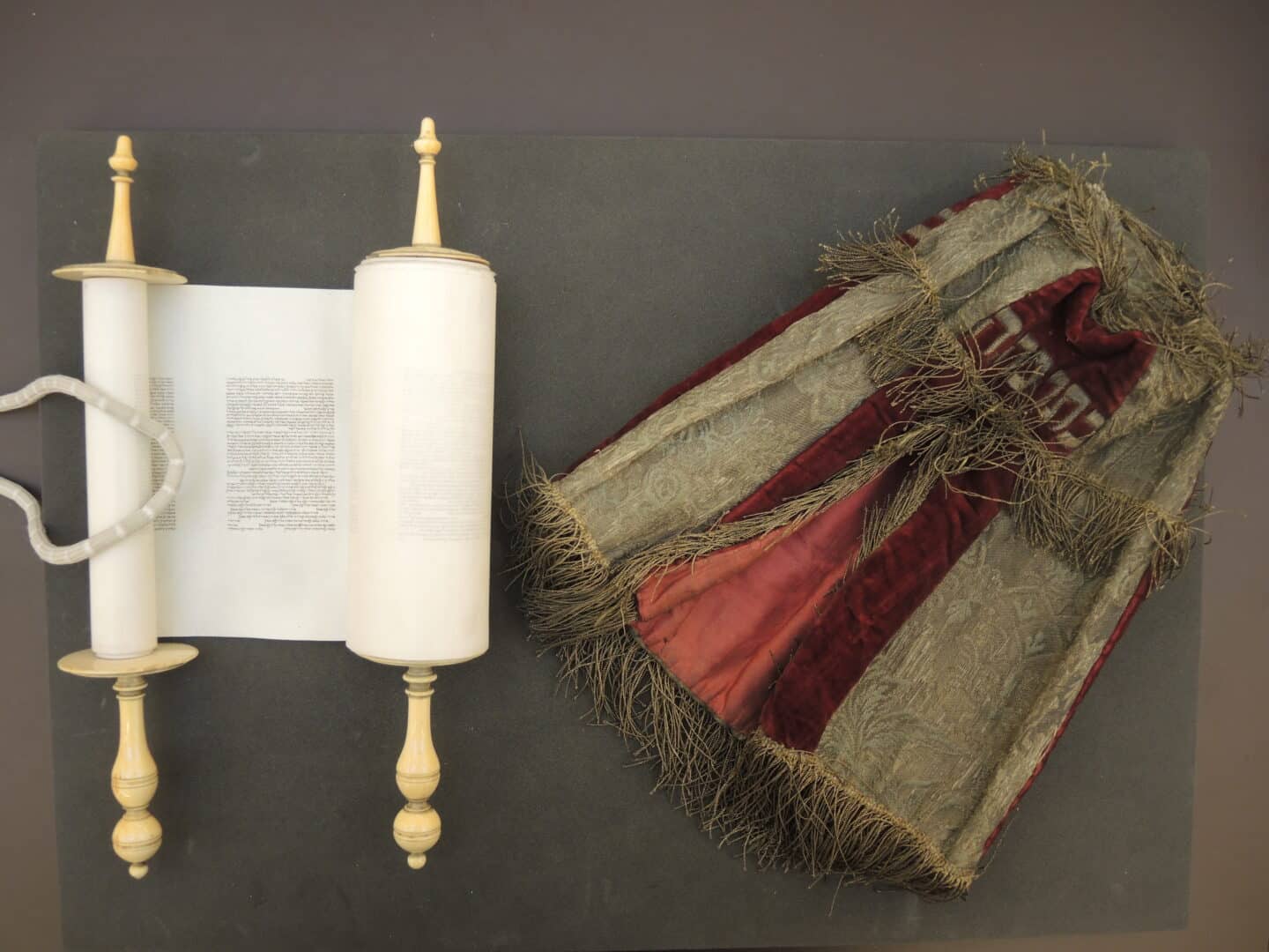 The parchment scroll, partially open, and its red and gold covering mantle are lying side-by-side