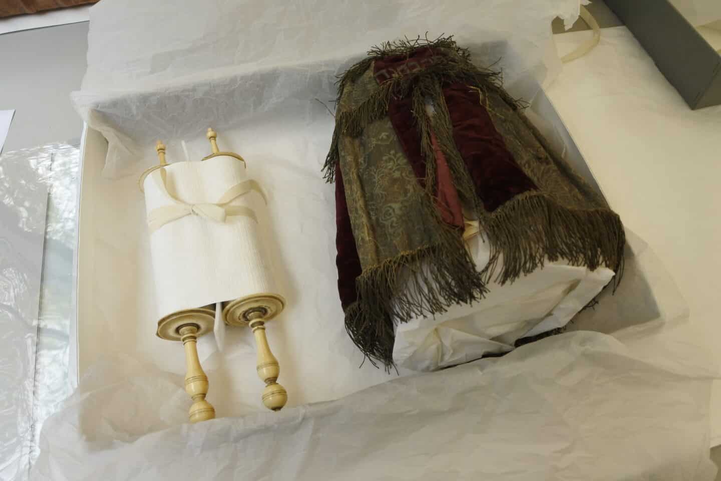 The mantle and scroll are pictured, housed in a box with a white tissue paper lining.