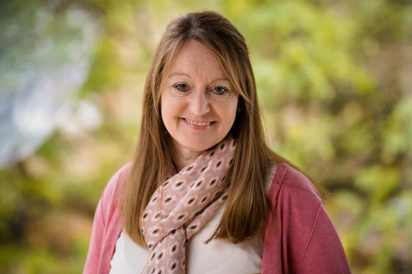 Headshot of Sue Williams, a woman in a white top, pink cardigan and scarf
