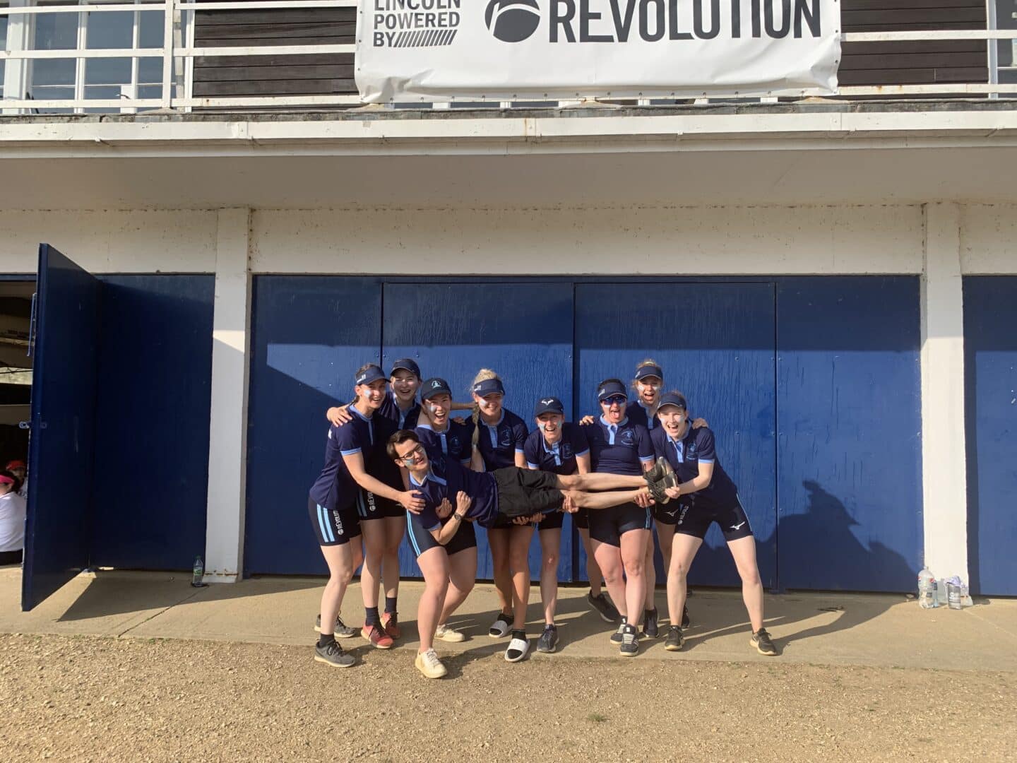 The W1 crew, smiling and holding up their cox.