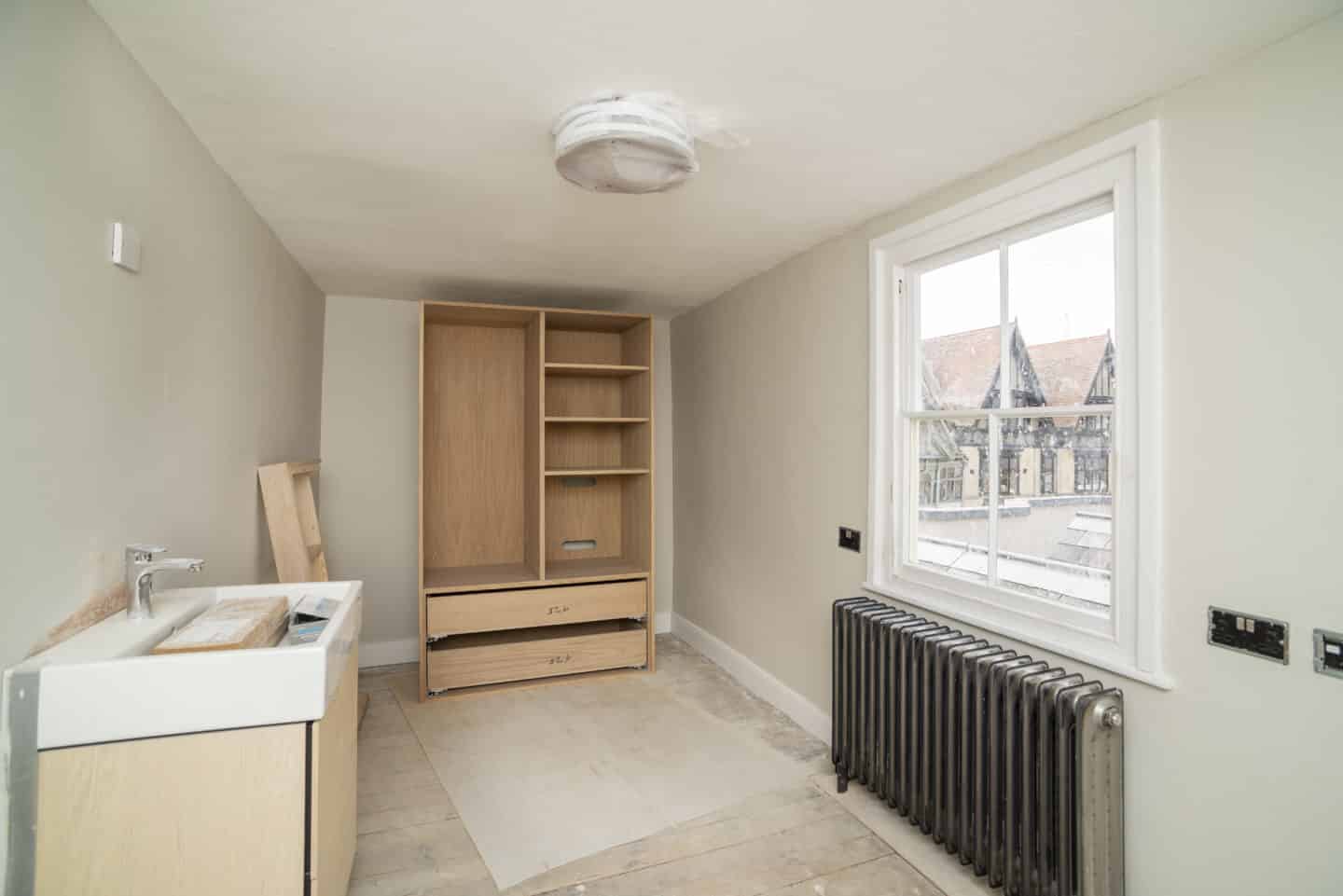 Room under construction, with a large wardrobe, a sink, a radiator, and a window overlooking the Mitre